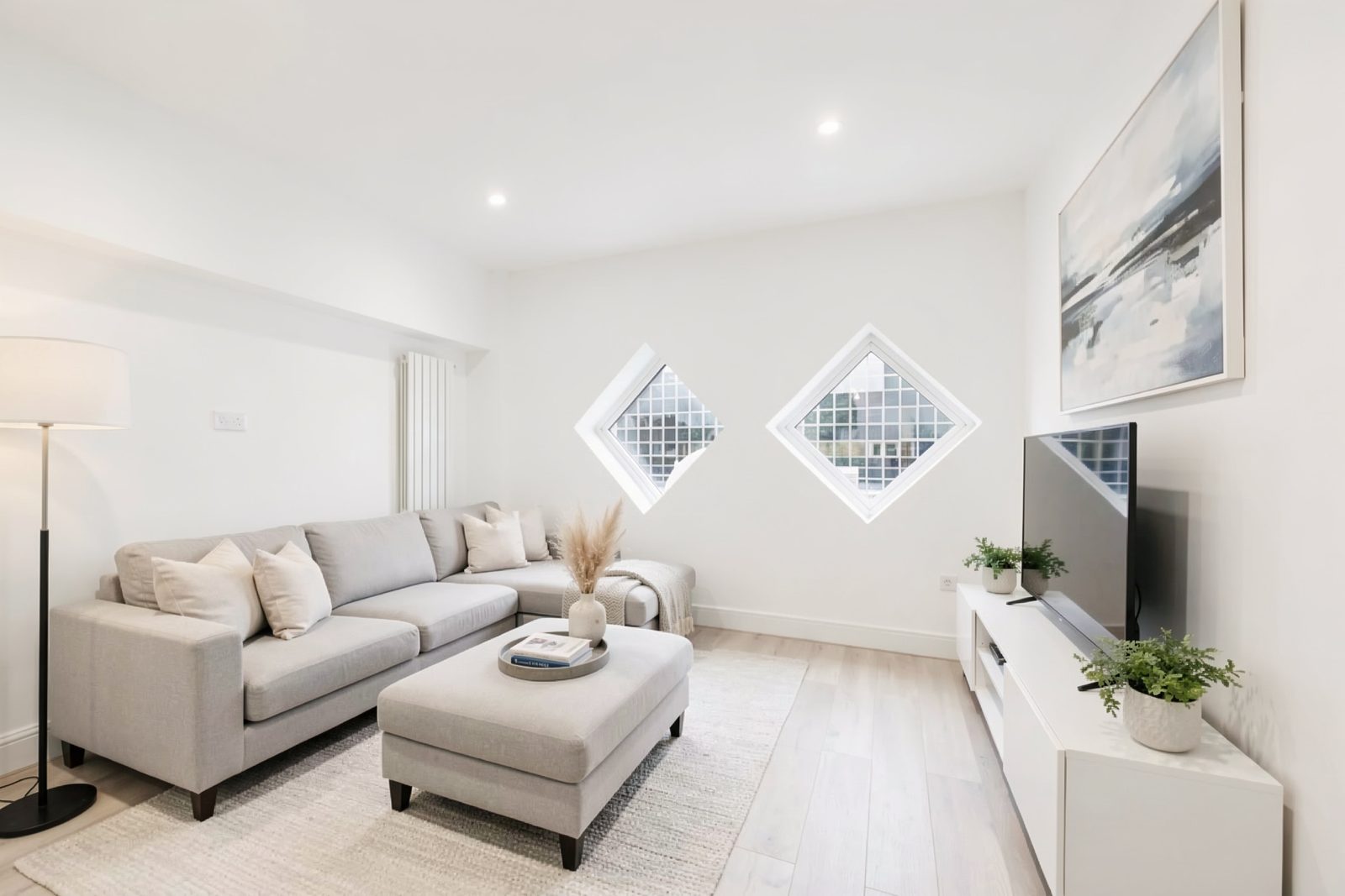 Living room with a grey corner sofa and two diamond-shaped windows in the end wall.